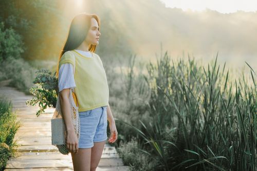 Free Woman wearing a yellow shirt and denim shorts standing on a sunny wooden pathway in nature. Stock Photo