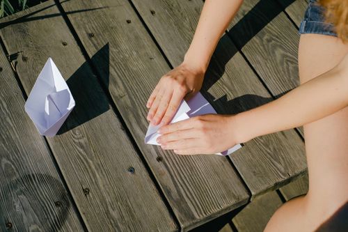 Free Hands folding paper boats on a wooden deck under the sun. Creative and peaceful outdoor activity. Stock Photo
