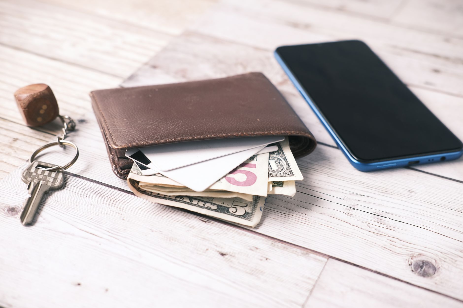 Close-up of a wallet with cash, smartphone, and keys on a wooden surface.