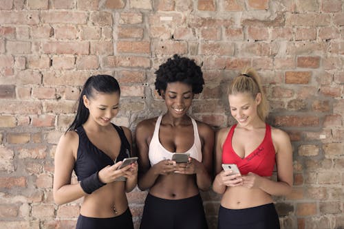 各种各样的颜色运动胸罩中的三个女人抱着，看着他们的智能手机