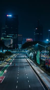 Illuminated skyscrapers of Jakarta at night with a lone motorcyclist on an empty highway.
