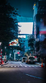 Vibrant city street scene at night with vehicles and illuminated billboards.