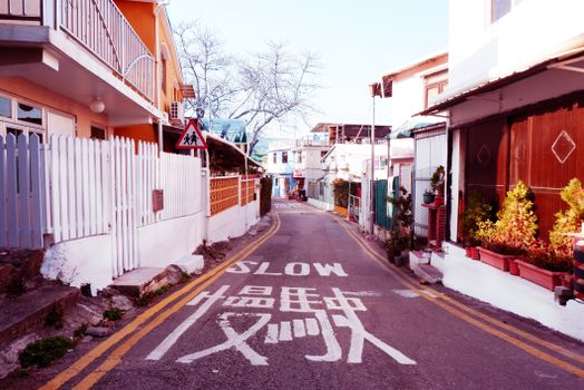 Quaint urban street scene in a Hong Kong residential area with colorful architecture and 'Slow' road markings.