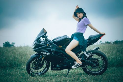 Free Fashionable woman in bucket hat sitting on a motorcycle in a field, showcasing style and adventure. Stock Photo