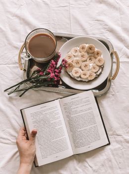 Flat lay of a morning scene with coffee, open book, and breakfast on a tray.