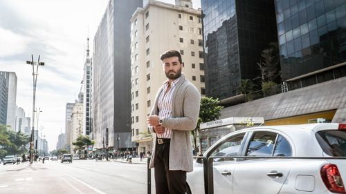 Free Fashionable man in urban São Paulo setting, wearing a striped shirt and grey cardigan. Stock Photo