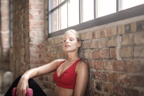 Free A young woman in activewear rests against a brick wall after exercising, showcasing fitness and dedication. Stock Photo