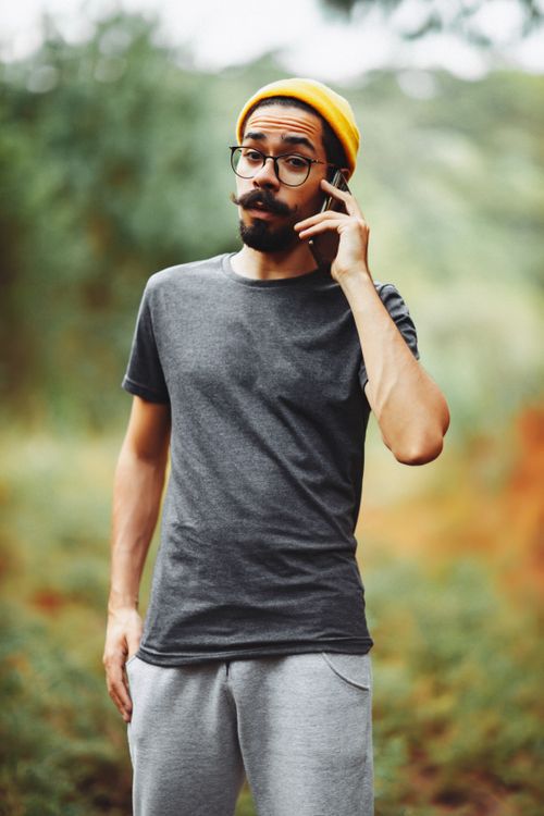 Free Portrait of a bearded man with eyeglasses and yellow beanie, talking on phone outdoors in casual wear. Stock Photo
