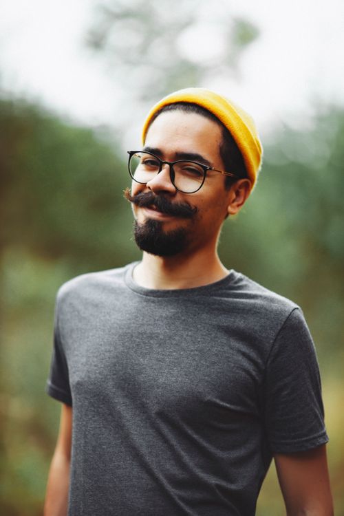 Free Stylish man with a beard and glasses smiling outdoors wearing a yellow beanie. Stock Photo