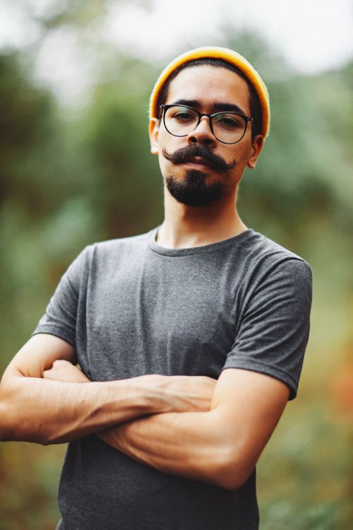 Free Portrait of a stylish bearded man with glasses wearing a yellow beanie and gray shirt outdoors. Stock Photo