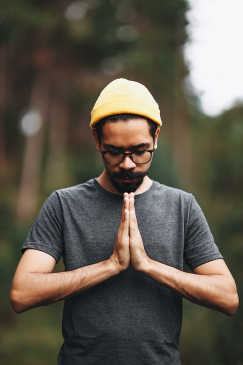 Free Man wearing a beanie meditating with closed eyes in a serene forest setting. Stock Photo