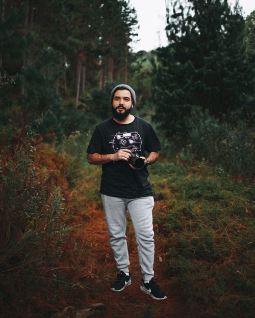 Free A bearded man holding a camera, standing in a lush forest, exuding a contemplative mood. Stock Photo