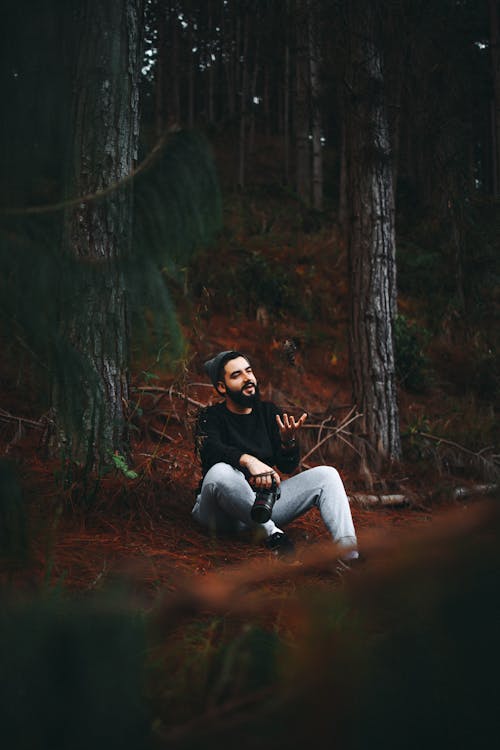 A Man Sitting in the Forest while Holding a DSLR Camera
