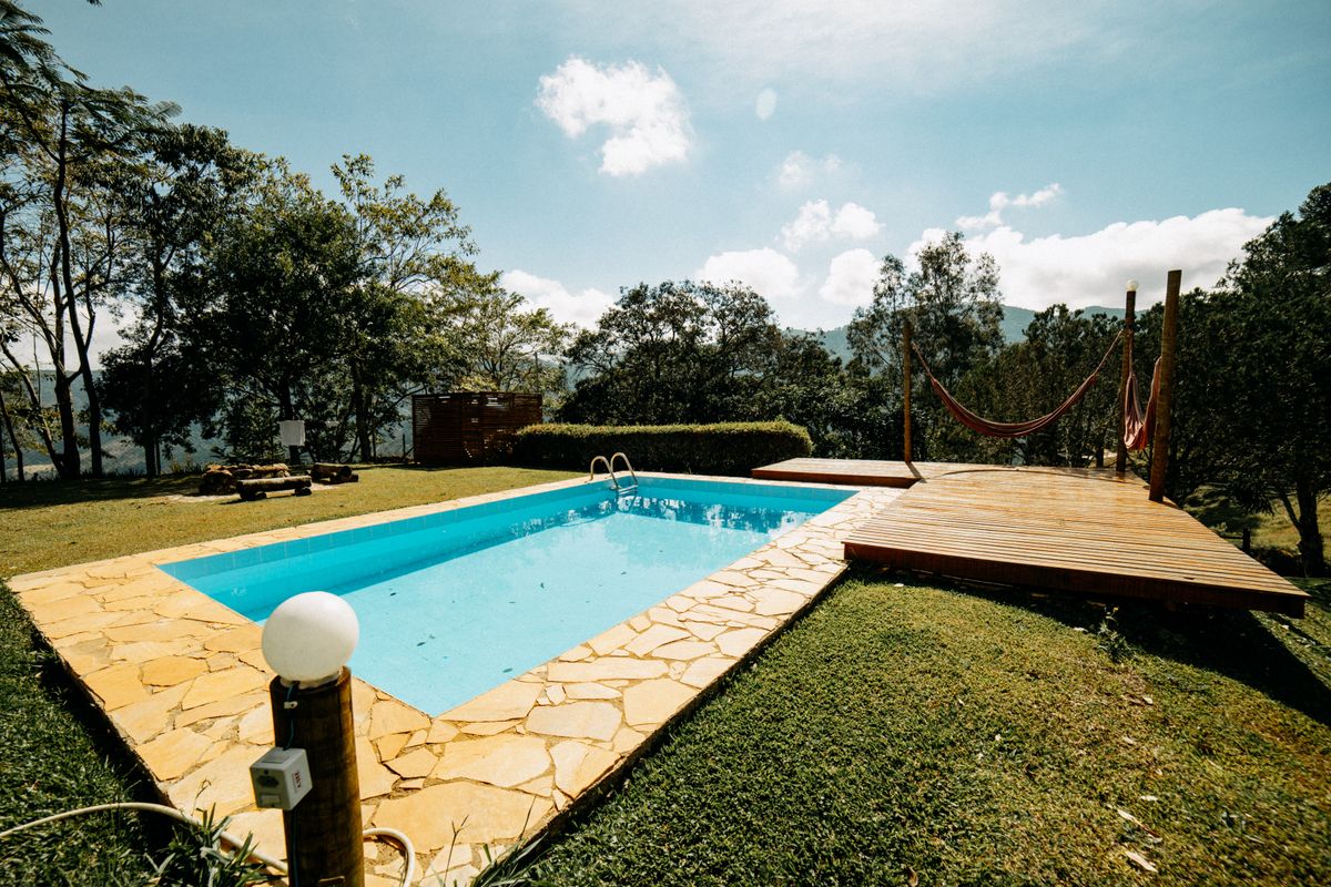 A serene outdoor pool with a wooden deck and hammock surrounded by lush greenery on a sunny day