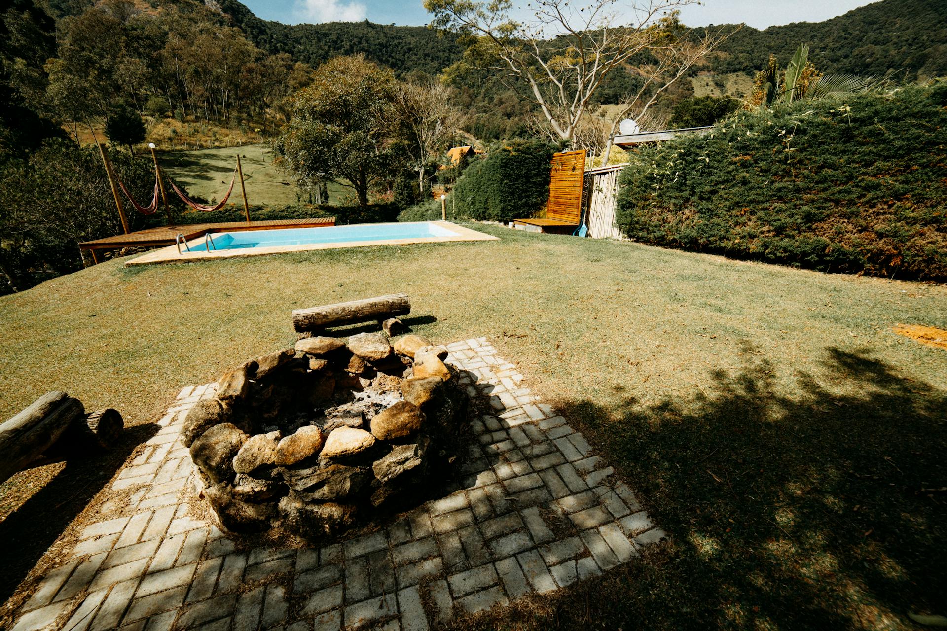 Tranquil outdoor space featuring a stone firepit and swimming pool in a lush garden.