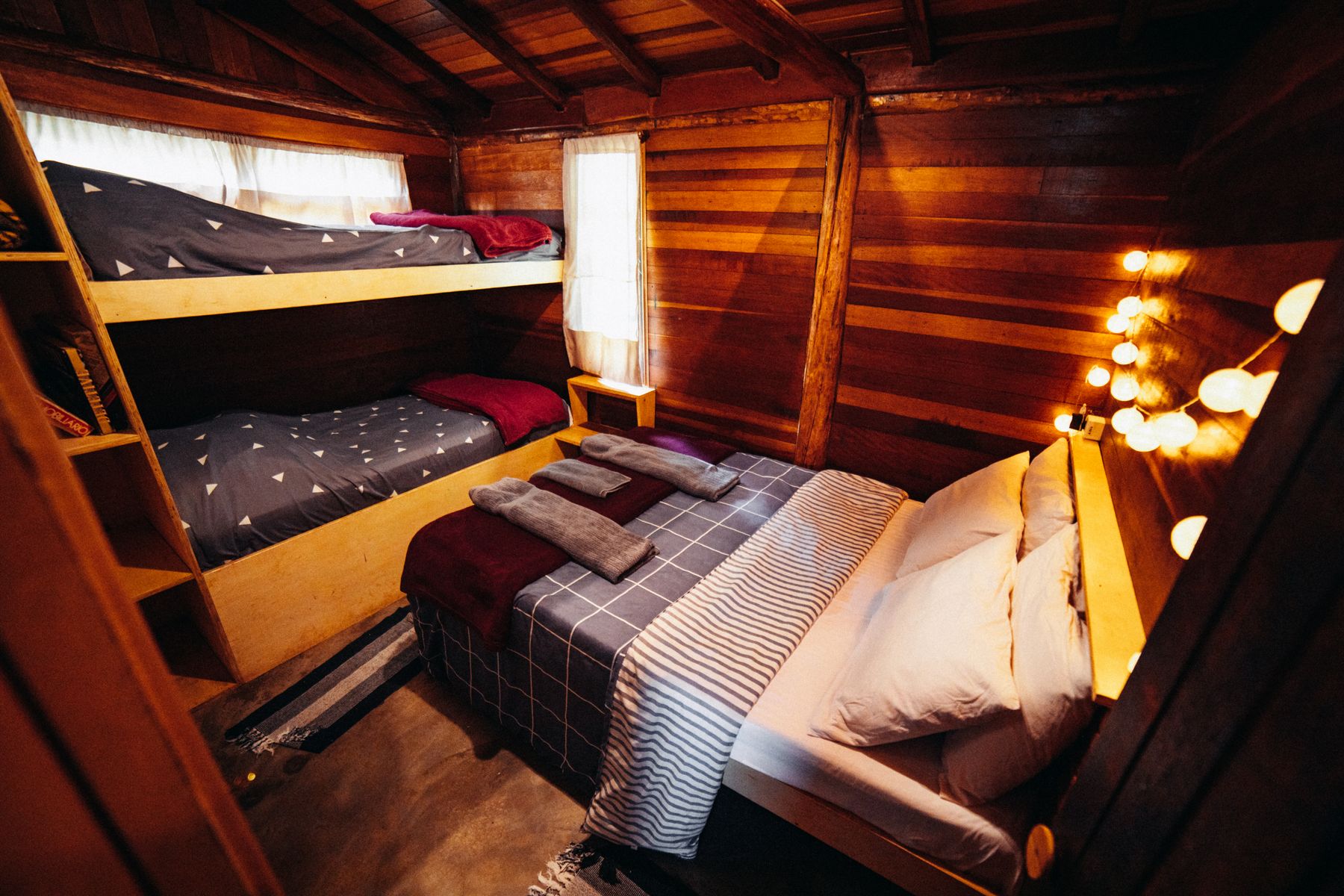 Compact wooden cabin bedroom with two beds, paneled walls, simple linens and warm lamps