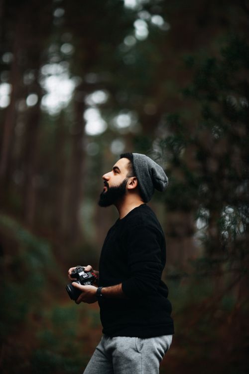 Free A bearded man wearing a beanie looks up contemplatively in a forest setting, creating a serene outdoor portrait. Stock Photo