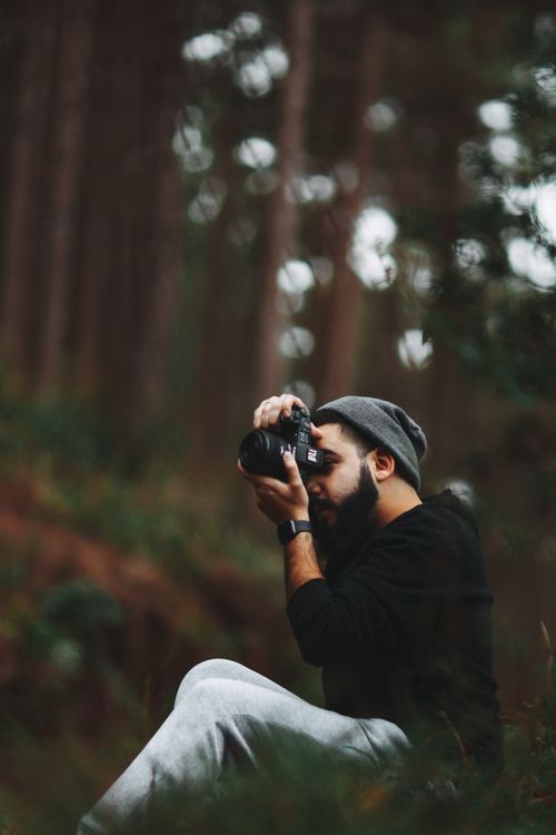 Free Bearded man in beanie photographing nature in lush forest setting. Stock Photo