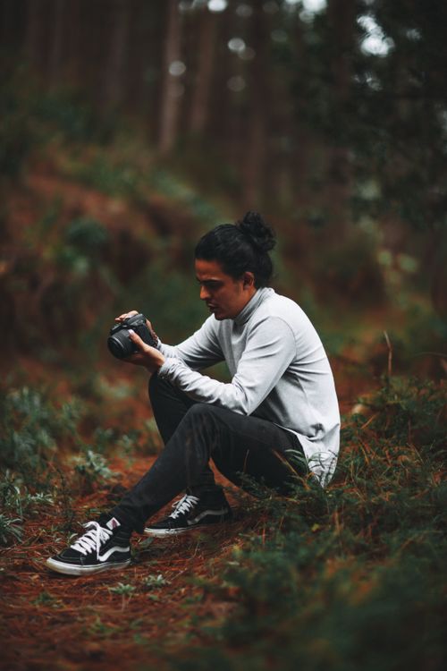 Free A man with a camera kneels in the forest, embracing his passion for nature photography. Stock Photo