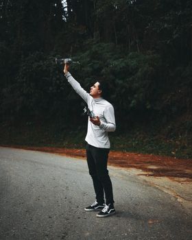 A man in a gray sweater controls a drone on a forest road, capturing the essence of technology in nature.