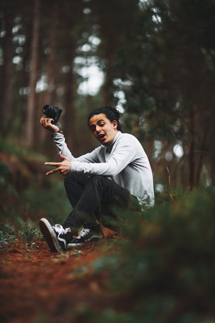 A Man in a Gray Sweater Squatting while Holding a Camera · Free Stock Photo