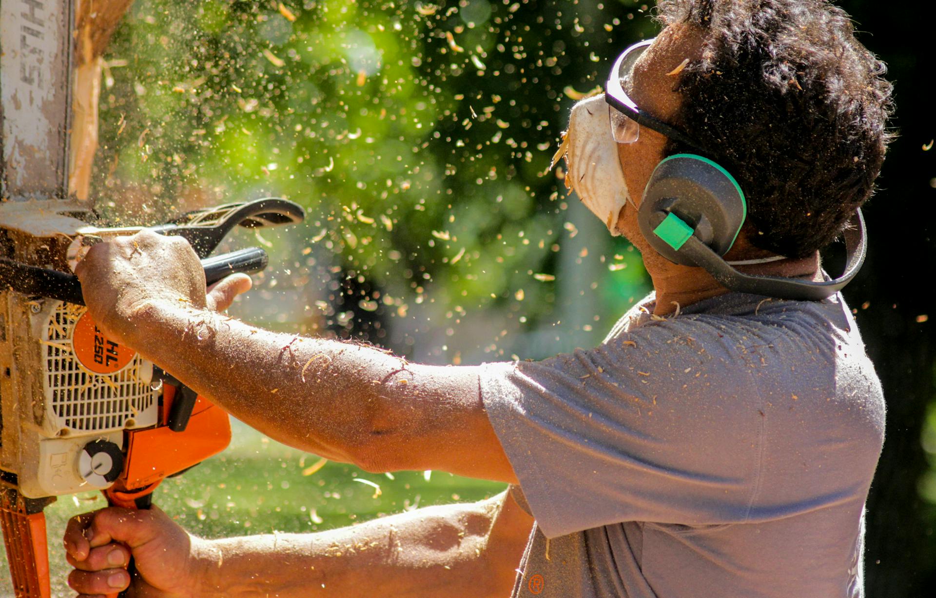 Man cutting wood with a chainsaw, wearing safety gear outdoors.