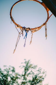 A weathered basketball hoop with frayed netting set against a twilight sky, symbolizing nostalgia and outdoor sports.