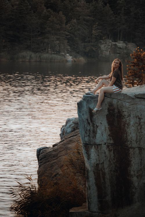 Free A woman sitting peacefully on a rock by the lake, evoking a calming atmosphere. Stock Photo
