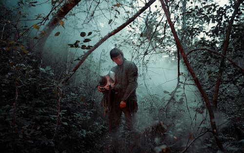 Man in Jacket Holding Helmet in the Forest 