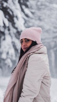 A woman wearing winter attire in a snowy forest, showcasing winter fashion with a beanie and scarf.