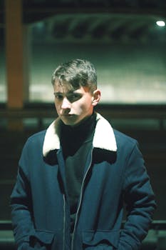 Serious young man posing in a jacket in a night setting with a blurred background.