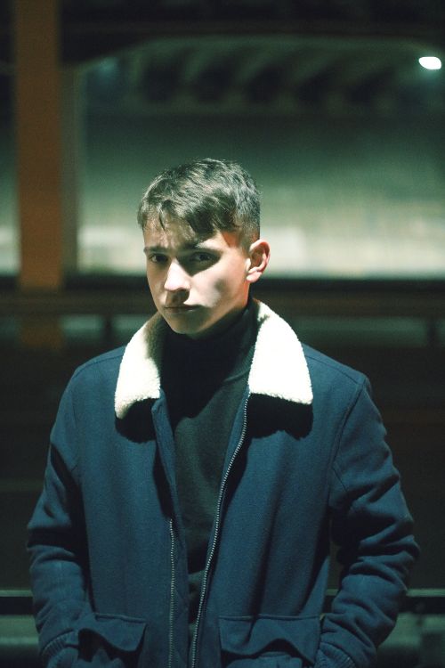 Free Serious young man posing in a jacket in a night setting with a blurred background. Stock Photo