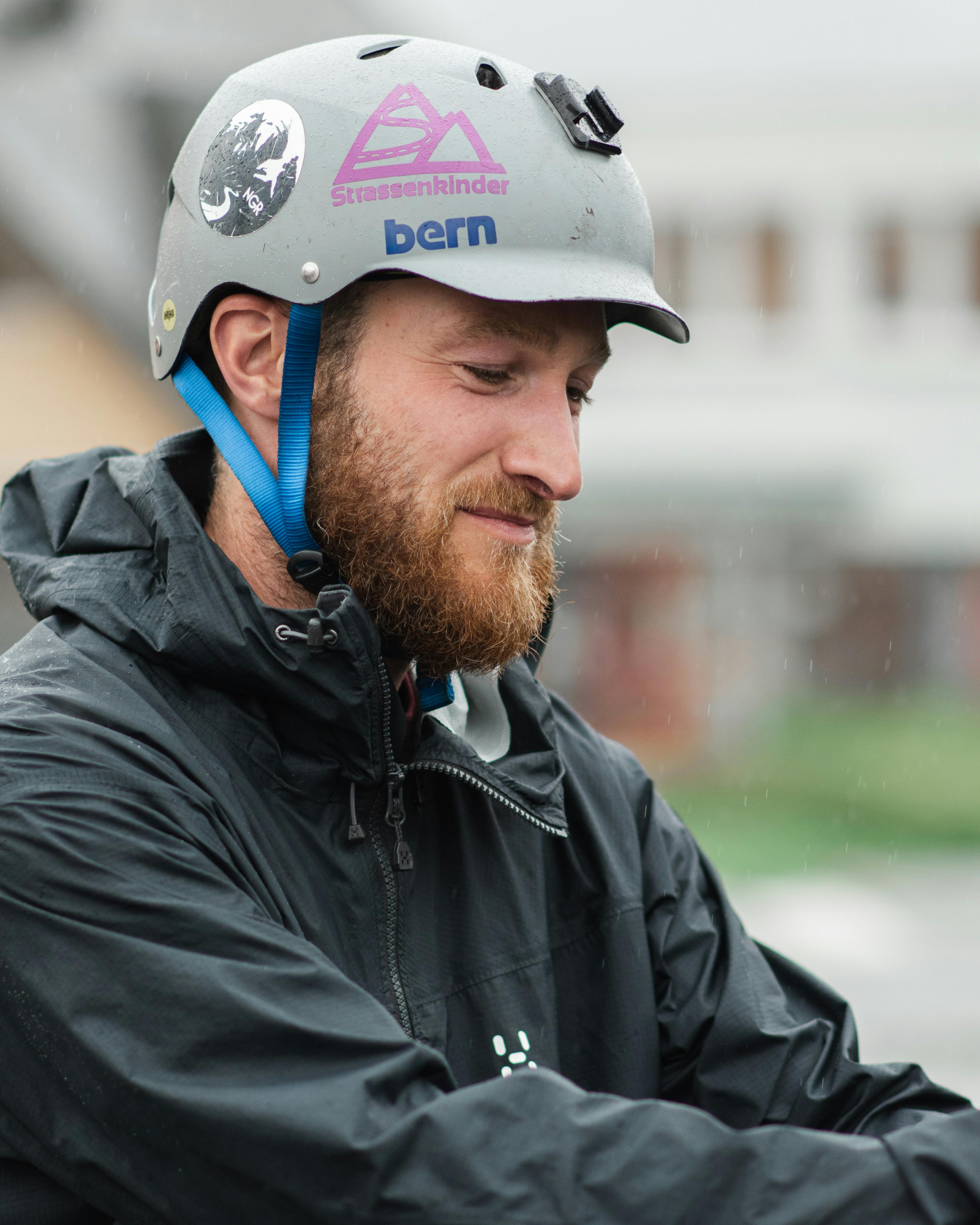 A man in a safety helmet and rain jacket standing outdoors with a thoughtful expression.