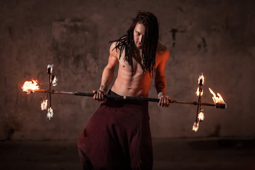 A Topless Man Holding a Stick With Fire