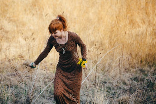 Woman in Brown Long Sleeve Dress Walking on Brown Grass Field