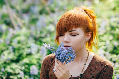 Free Serene young woman with eyes closed holding and smelling delicate spring flowers. Stock Photo