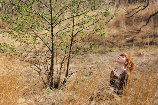 A serene scene with a woman relaxing beside a budding tree in a grassy field.
