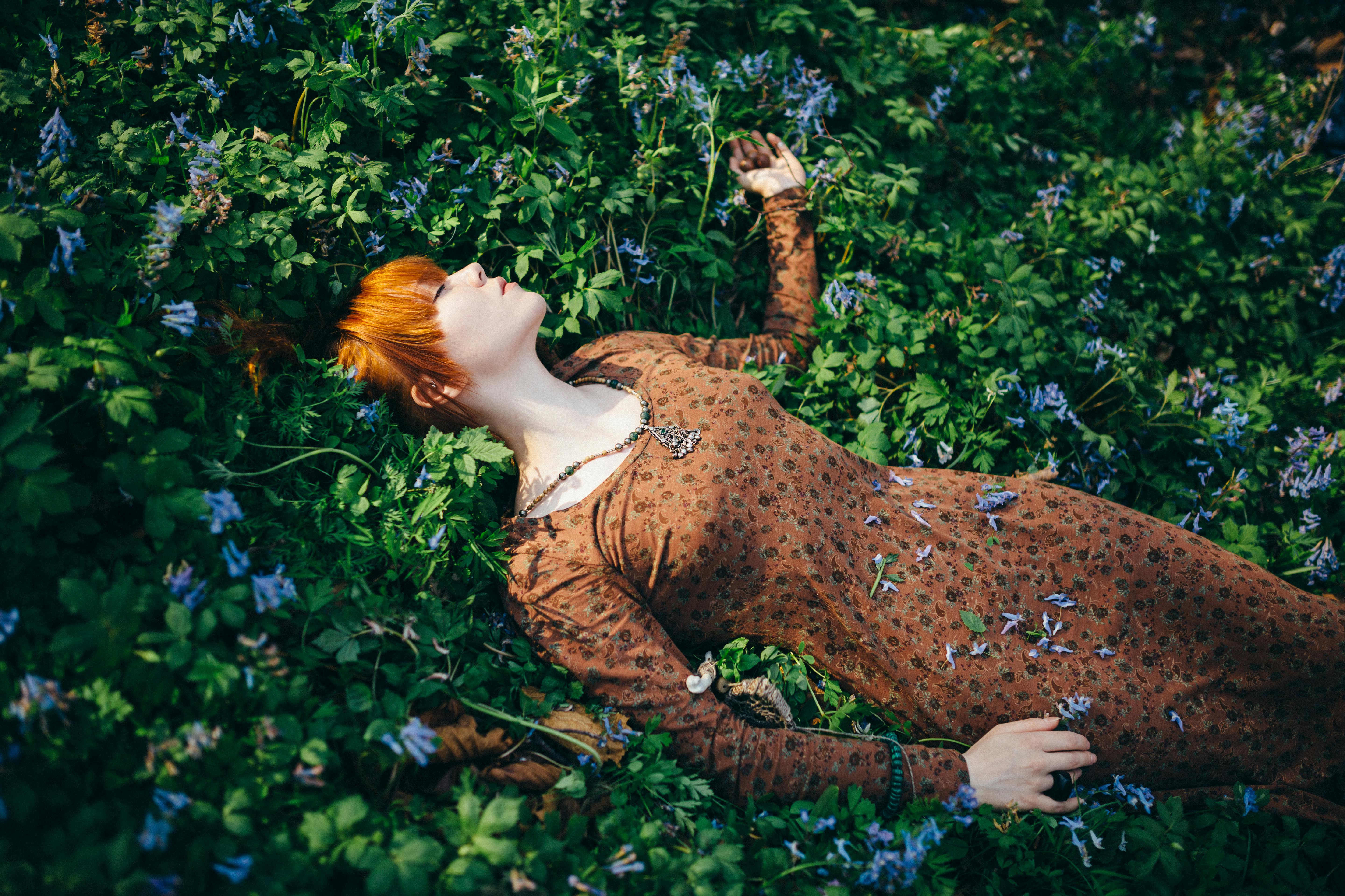 Woman with red hair lying peacefully in a field of blooming flowers.