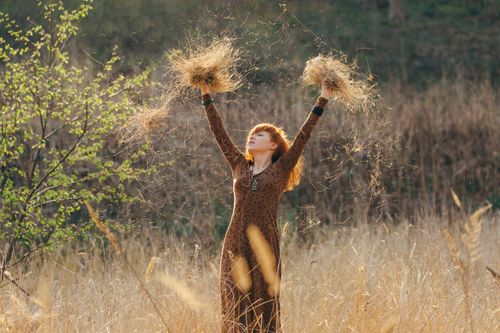 Free A woman in a brown dress joyfully throws dried grass in the air in a sunlit field. Stock Photo