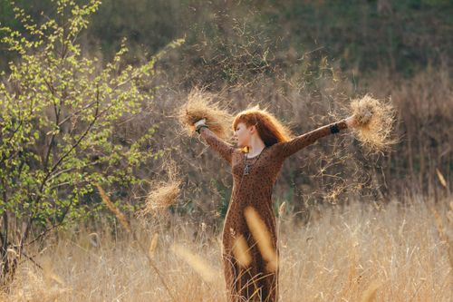 Free A woman in a brown dress joyfully throws dry grass in a sunlit field. Stock Photo