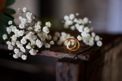 Gold Ring Bands and White Flowers Laid on a Wooden Stand