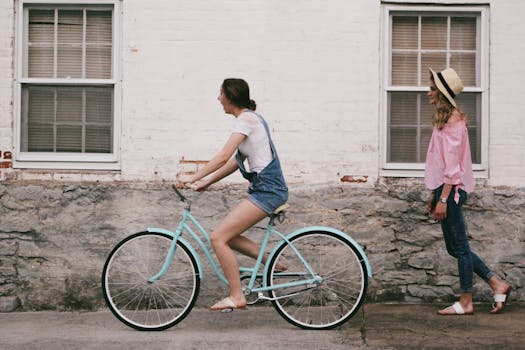 Two young women enjoy a friendly bike ride on a sunny urban street, showcasing fun and friendship.