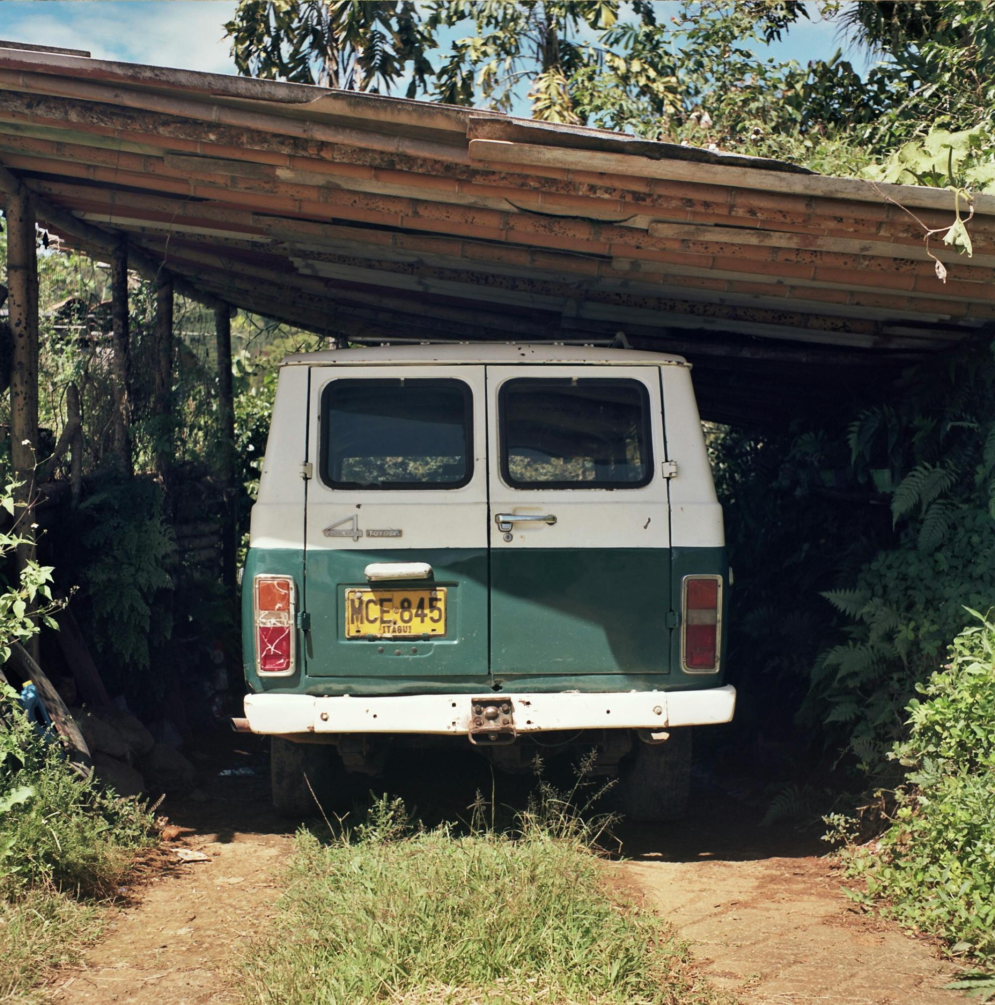 Classic van parked under a wooden shelter with green surroundings, showcasing rustic charm.