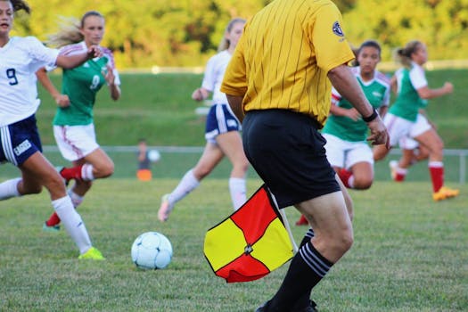 Women's soccer match featuring players and referee on field in motion.