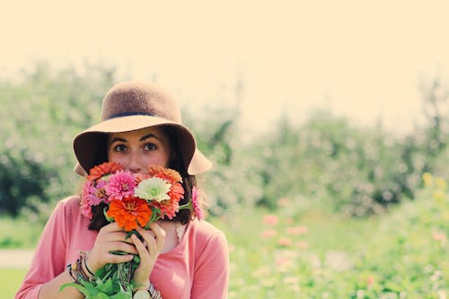 無料 帽子をかぶって、植物に囲まれた花を持っている女性 写真素材
