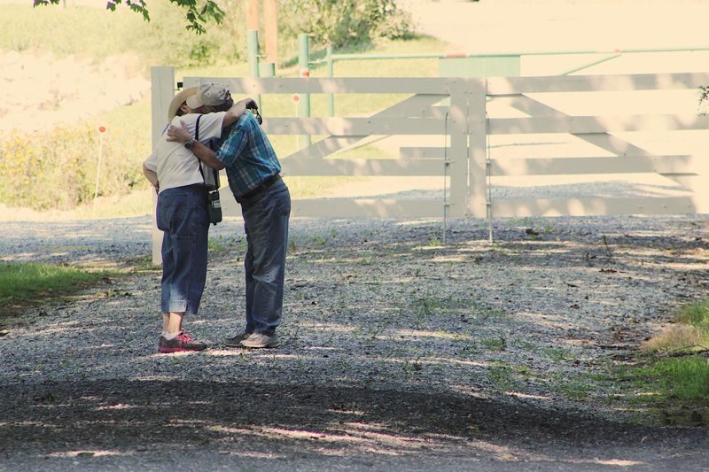 Two seniors embracing on a sunny day in a serene park.