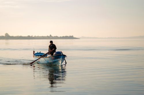 Free Fisherman rowing a boat on peaceful waters at dawn in Türkiye, capturing tranquility. Stock Photo