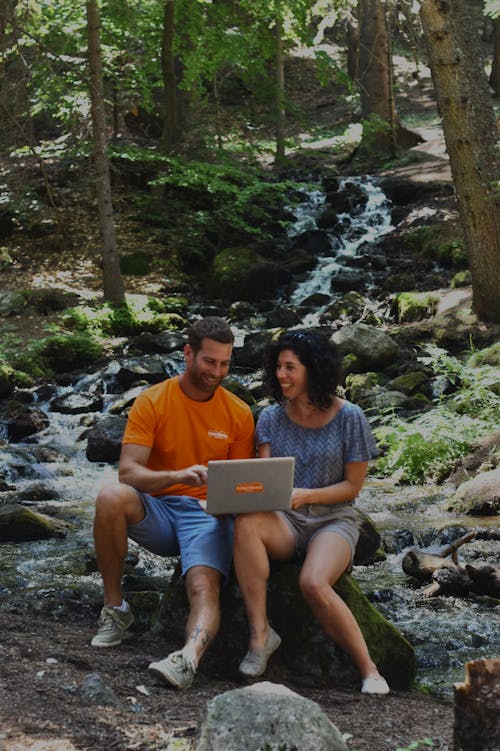 Couple Sitting on Rock While Using a Laptop
