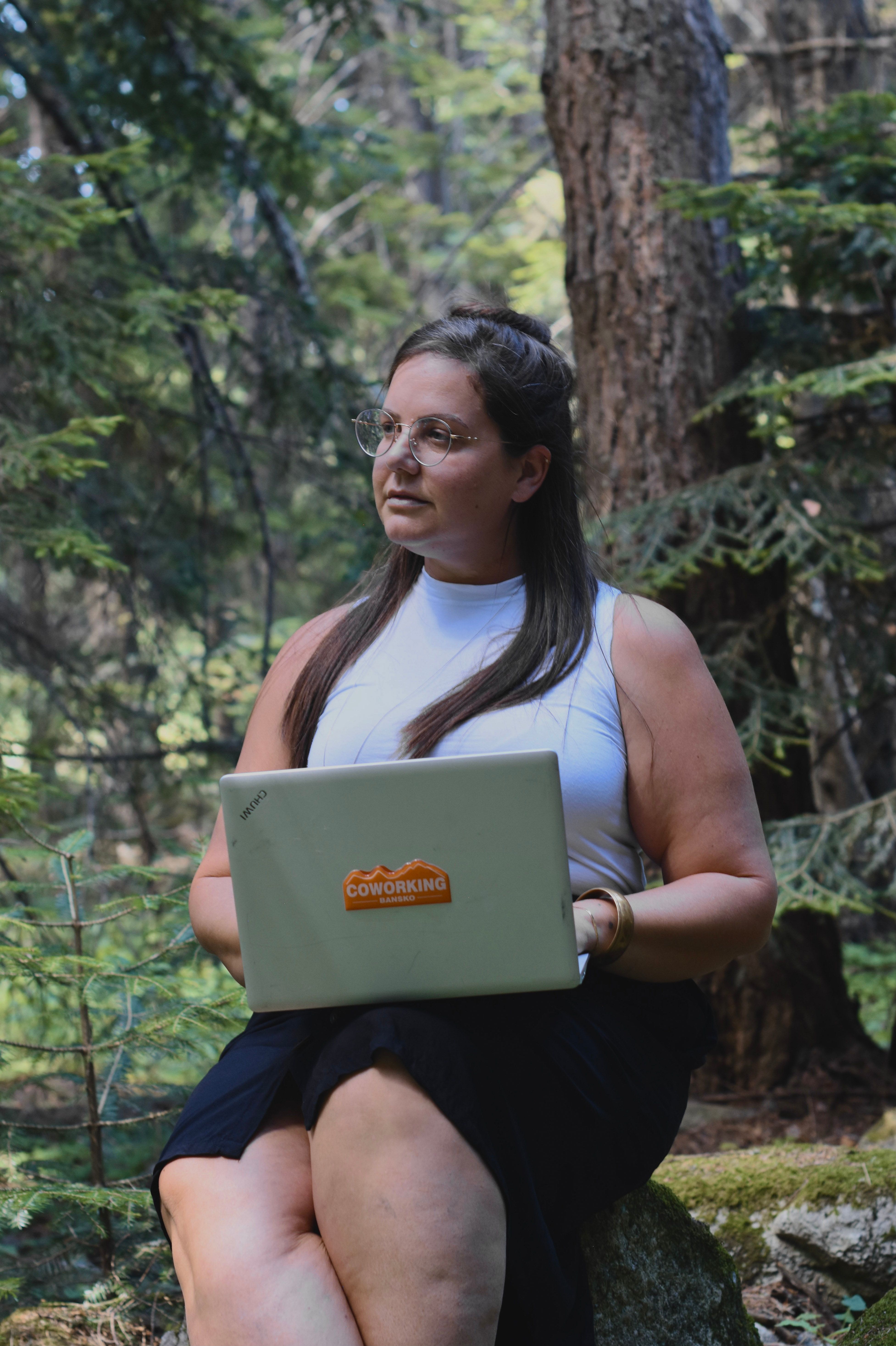 Woman using a laptop in a forest, representing digital nomad lifestyle