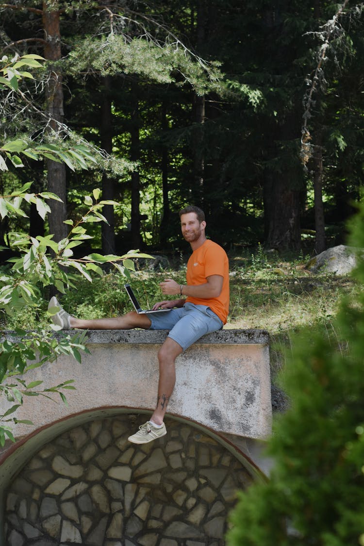 Man Wearing Orange Shirt Sitting On Concrete Platform In The Woods